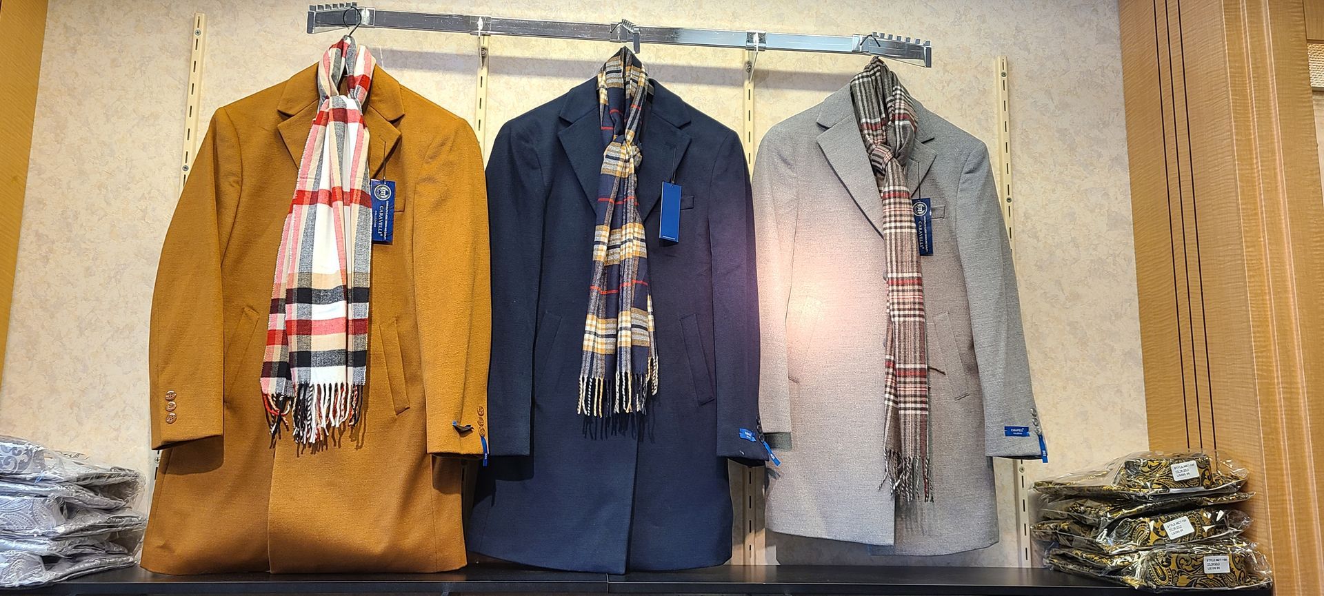 Three hanging outfits in tan, blue, and gray, each with a patterned scarf, displayed on a rack.