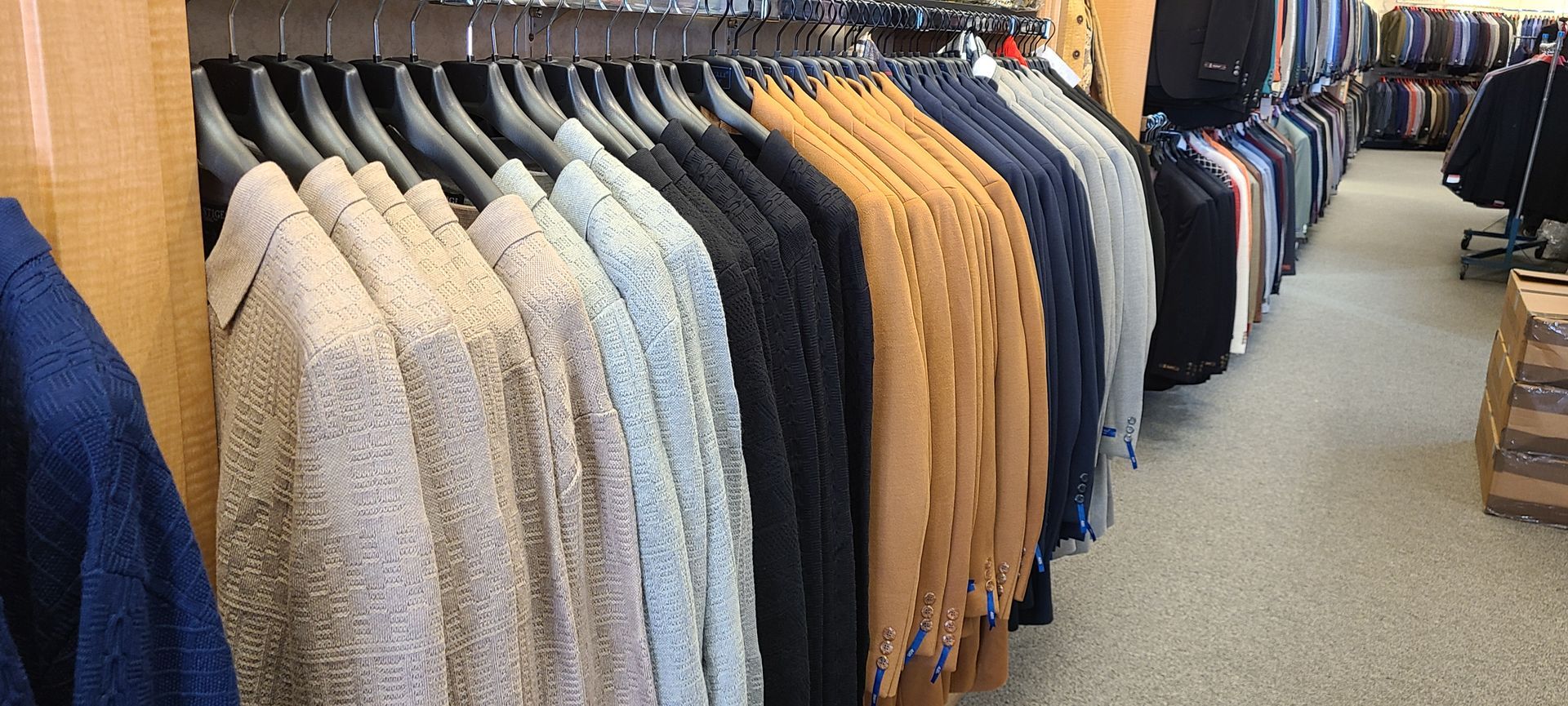 Clothing store aisle with rows of hanging jackets and sweaters in neutral tones and blue pants