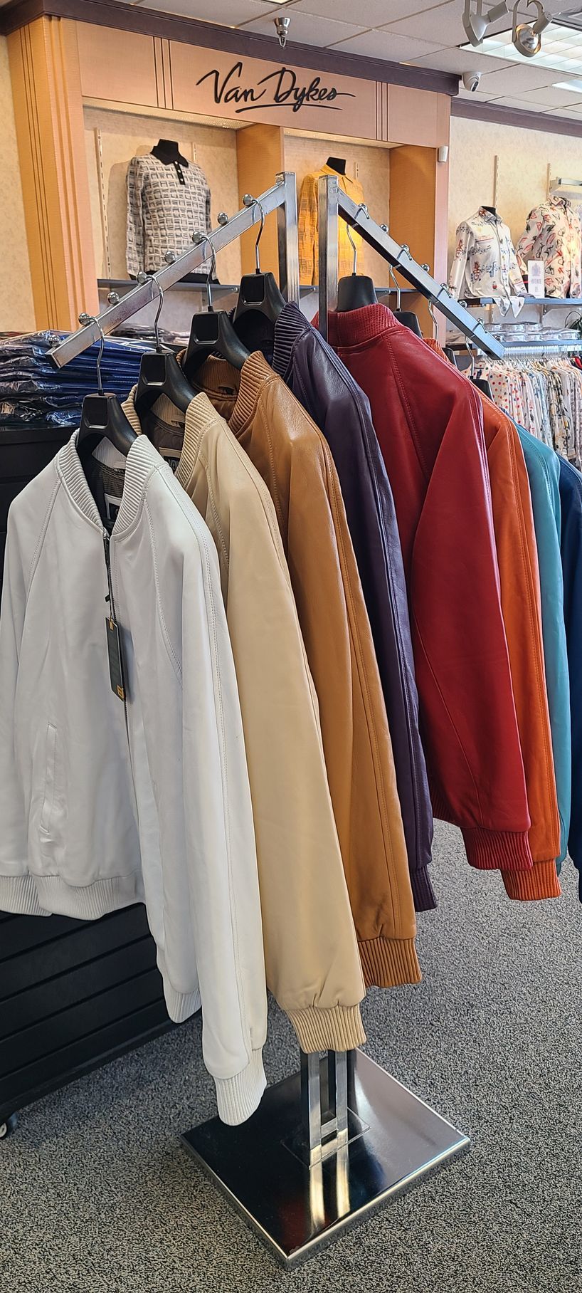 Clothing rack with assorted coats and jackets in white, beige, red, and blue at an outdoor market