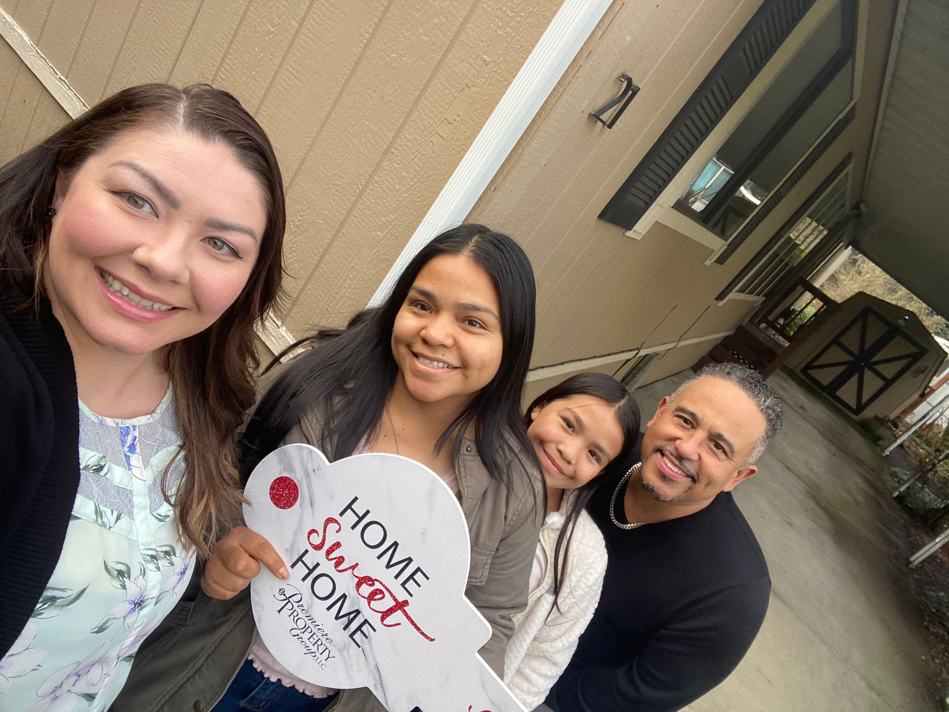 A family is standing in front of a house holding a home sweet home sign.