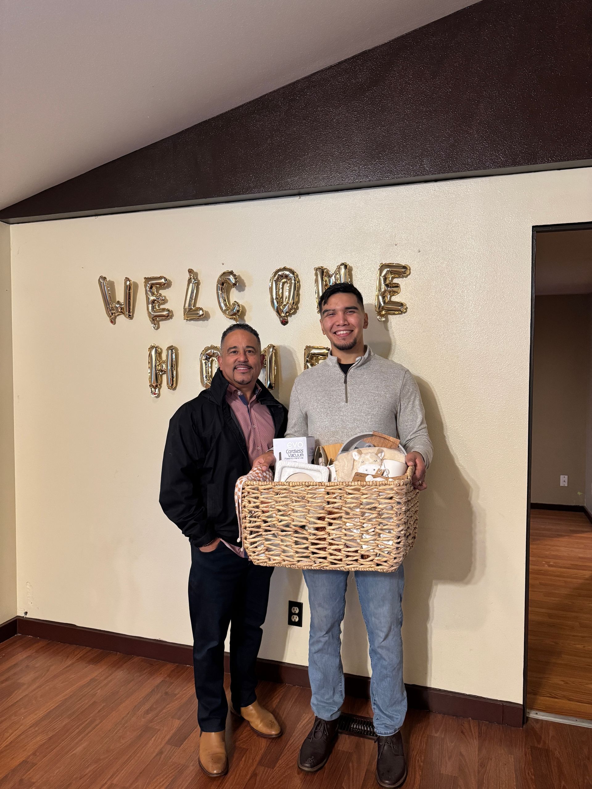 Two men are standing in front of a wall that says welcome home