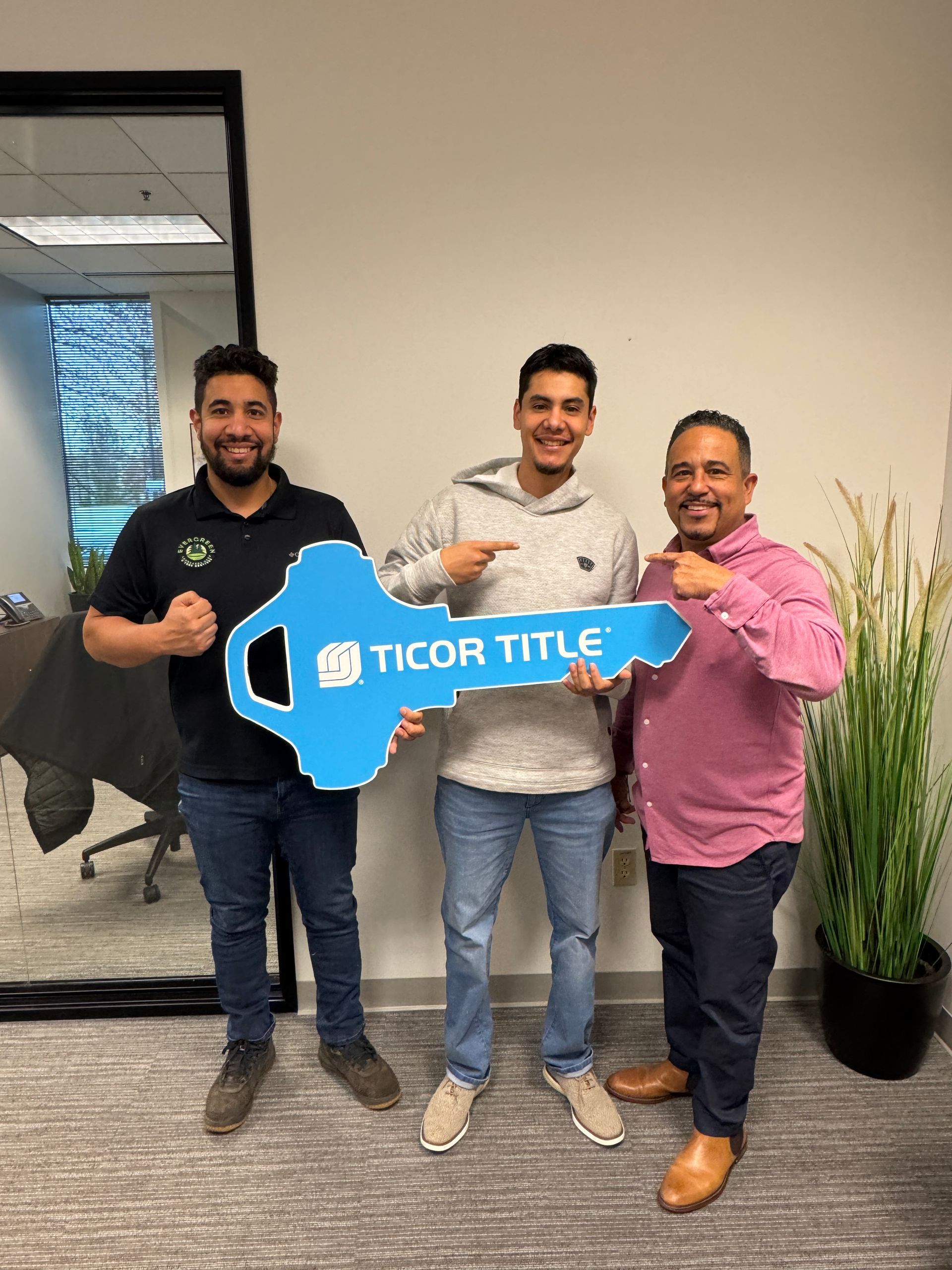 Three men are standing next to each other holding a large blue key.