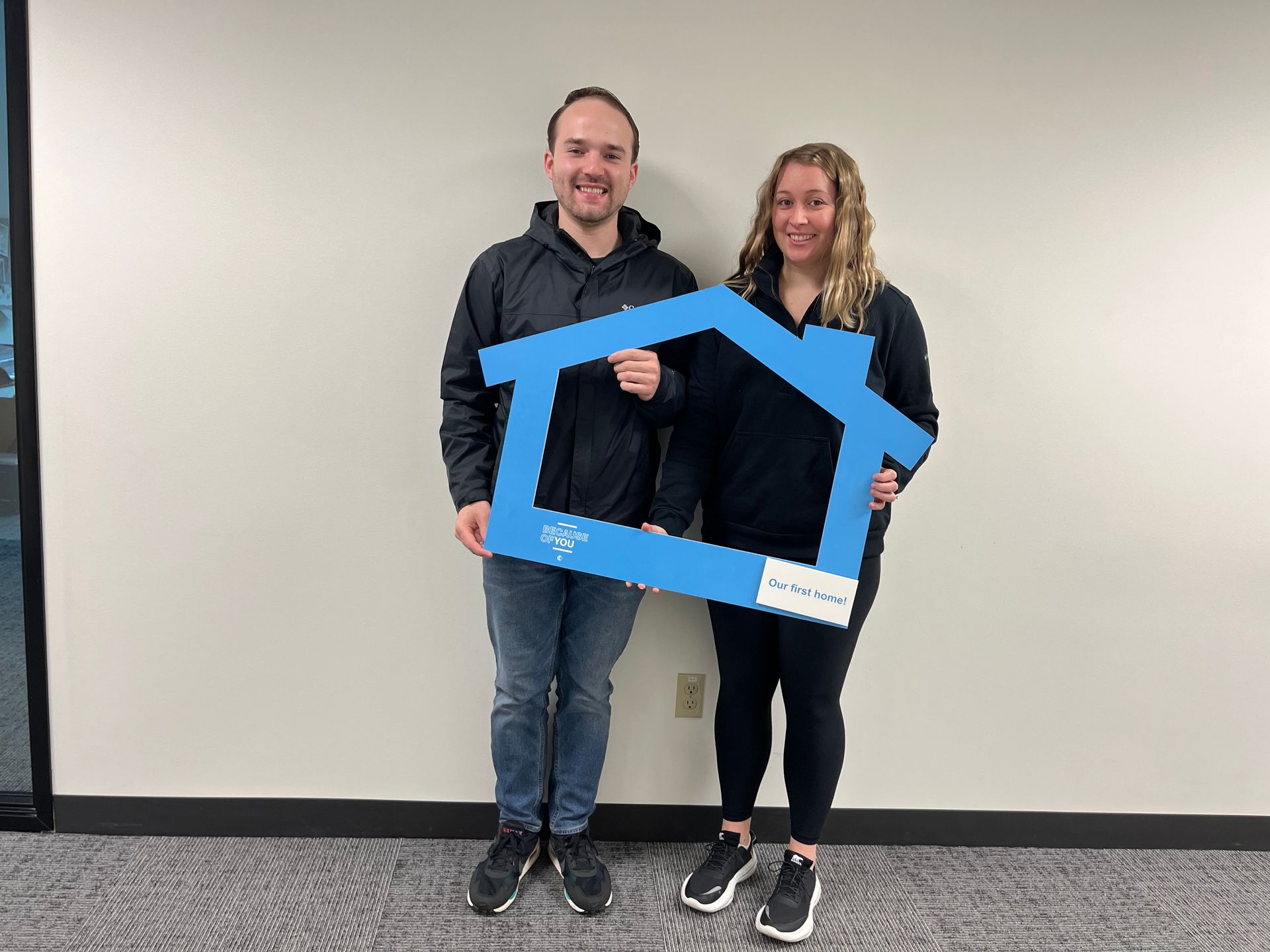 A man and a woman are holding a picture frame in the shape of a house.