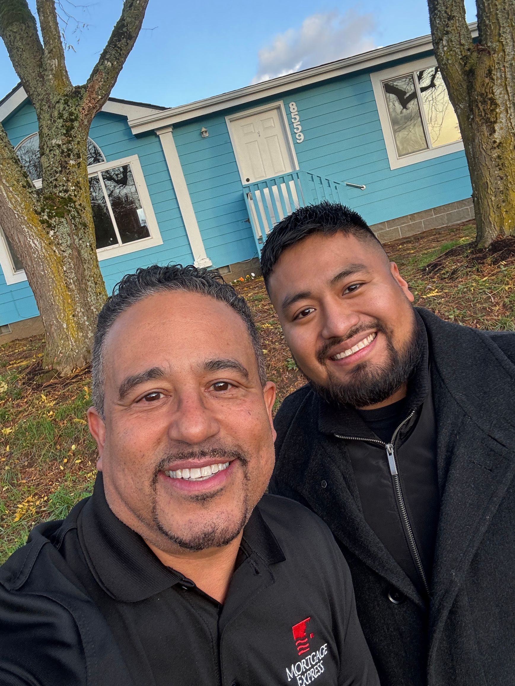Two men are posing for a picture in front of a blue house.