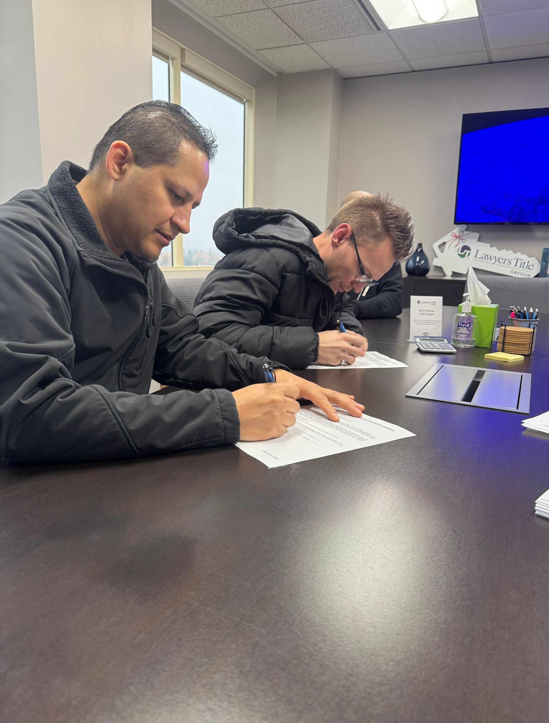 Two men are sitting at a table writing on papers.