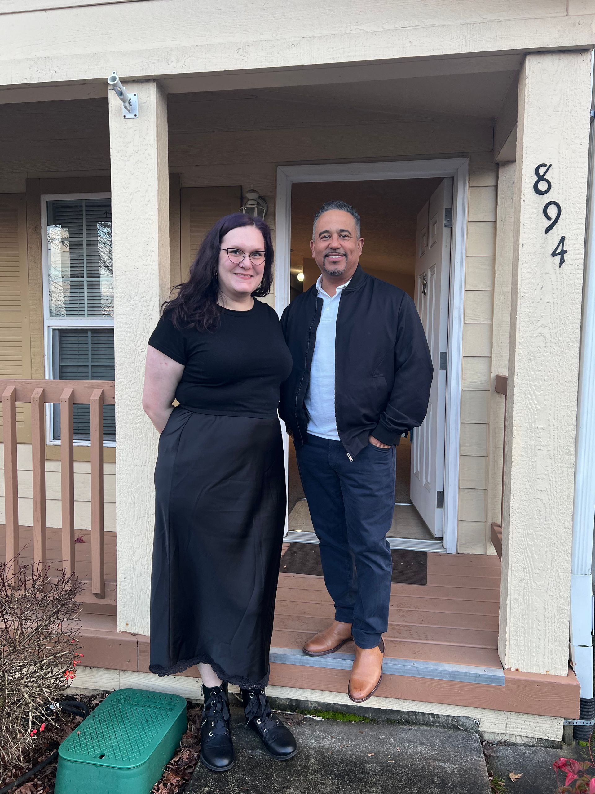 A man and a woman are standing in front of a house