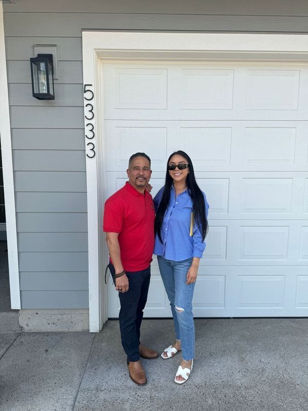 A man and a woman are standing in front of a garage door.