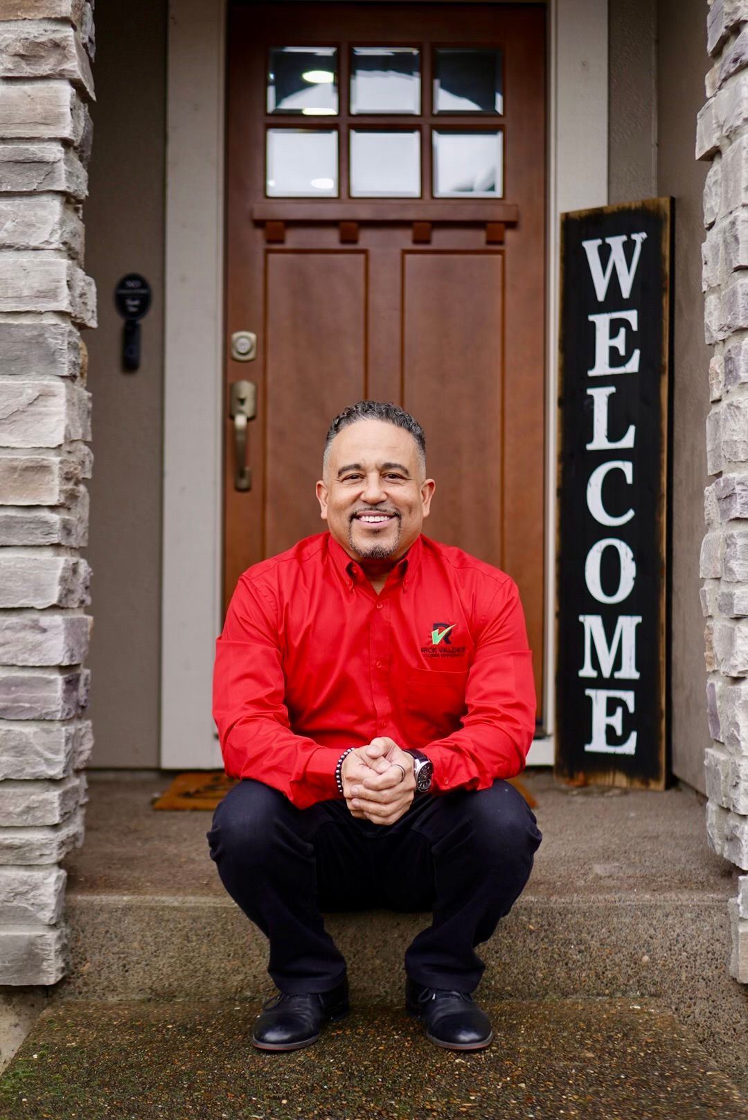 A man in a red shirt sitting in front of a house