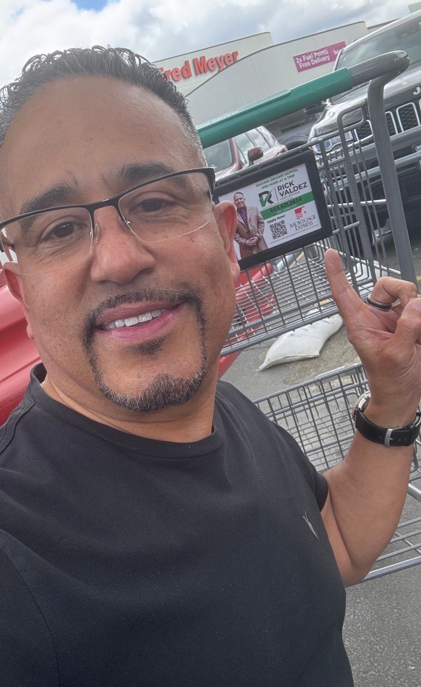 A man wearing glasses is holding a cell phone in front of a store.