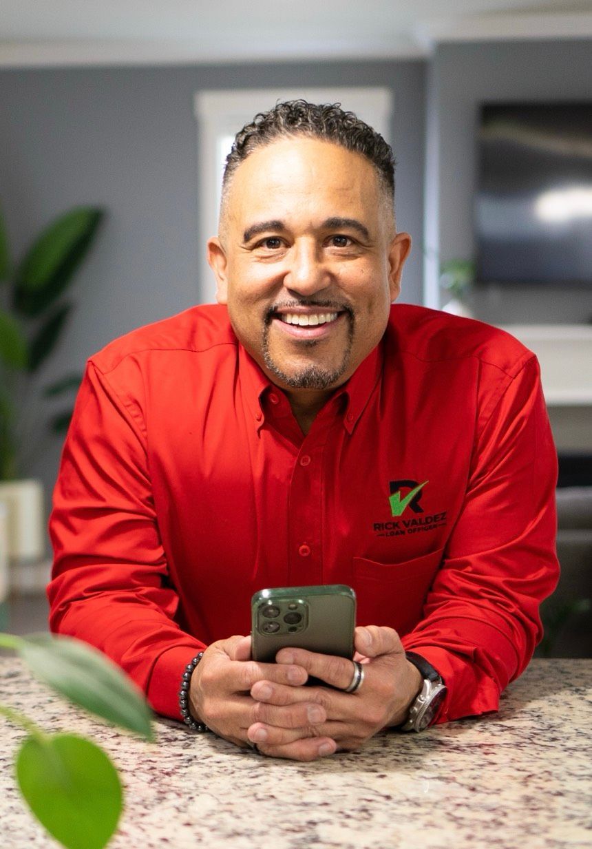A man in a red shirt is sitting on a counter holding a cell phone.