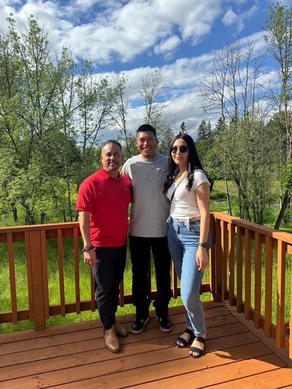 Three people are posing for a picture on a wooden deck.
