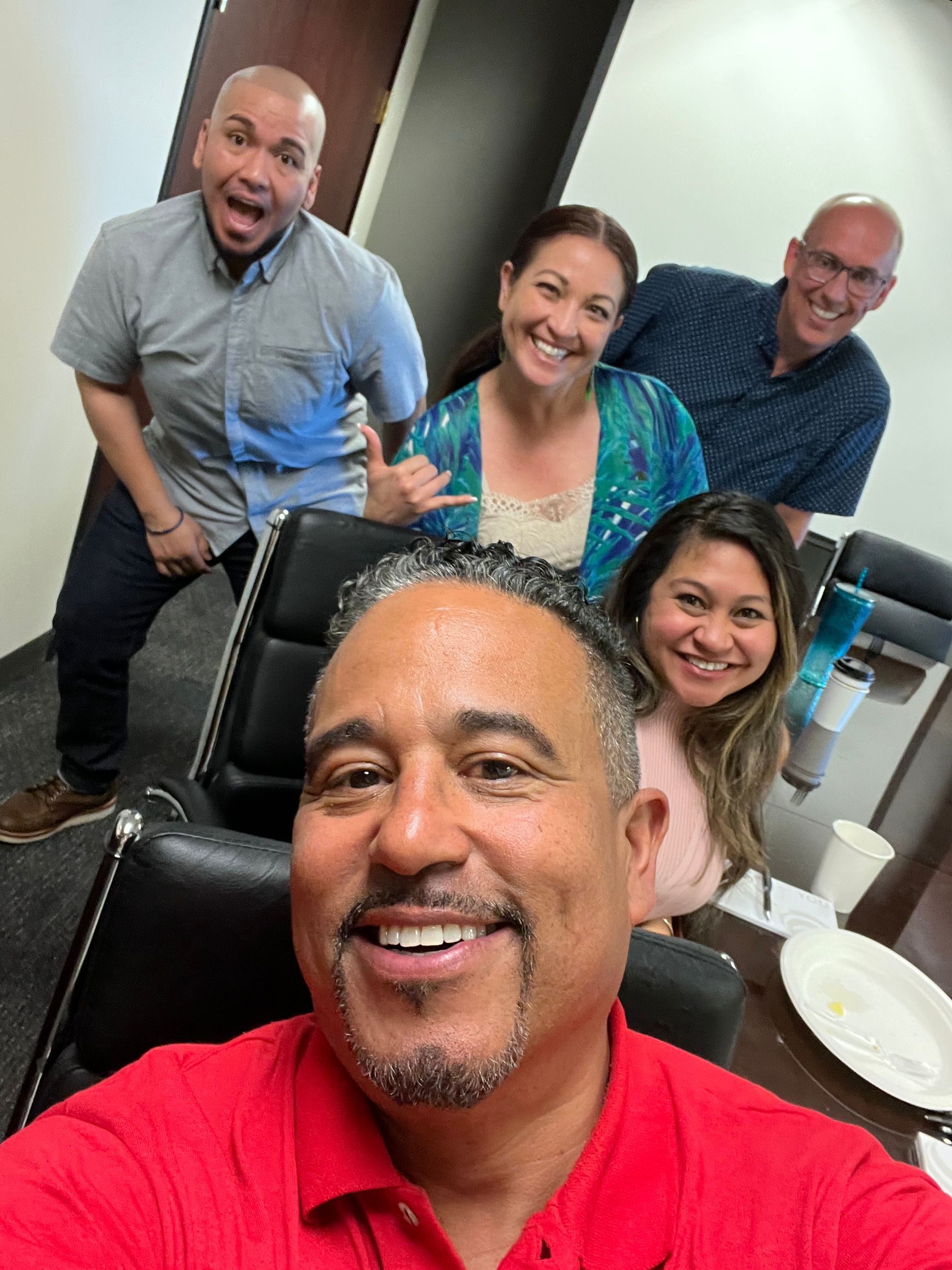 A man in a red shirt is taking a selfie with a group of people.