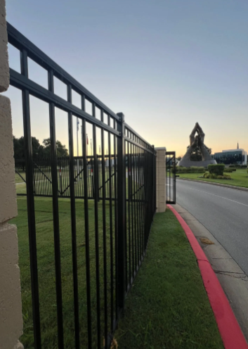 A black metal fence runs alongside a road with a painted red curb, leading toward a distant sculptural monument.