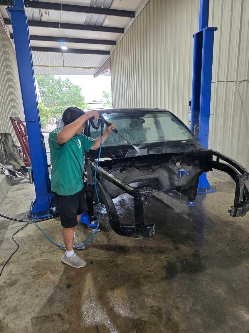 Person washing a black car in an indoor auto bay with blue lift posts.