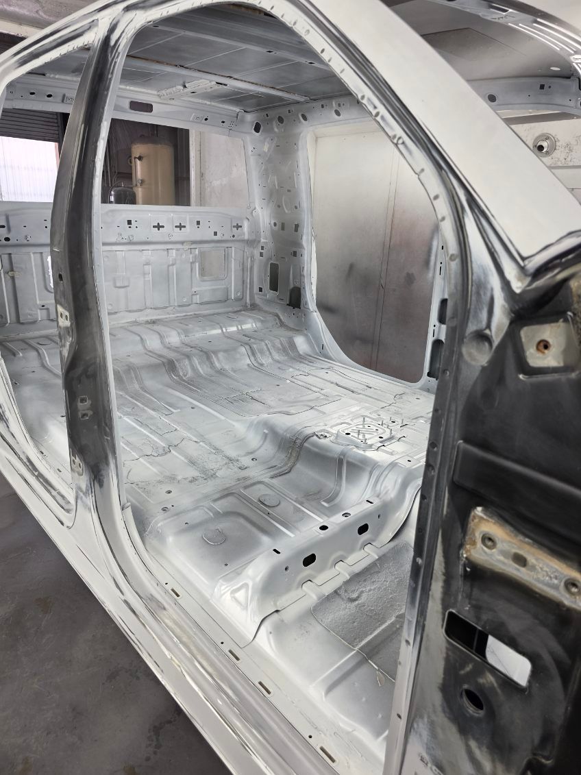Stripped car interior shell with bare metal and gray primer, viewed through an open side door