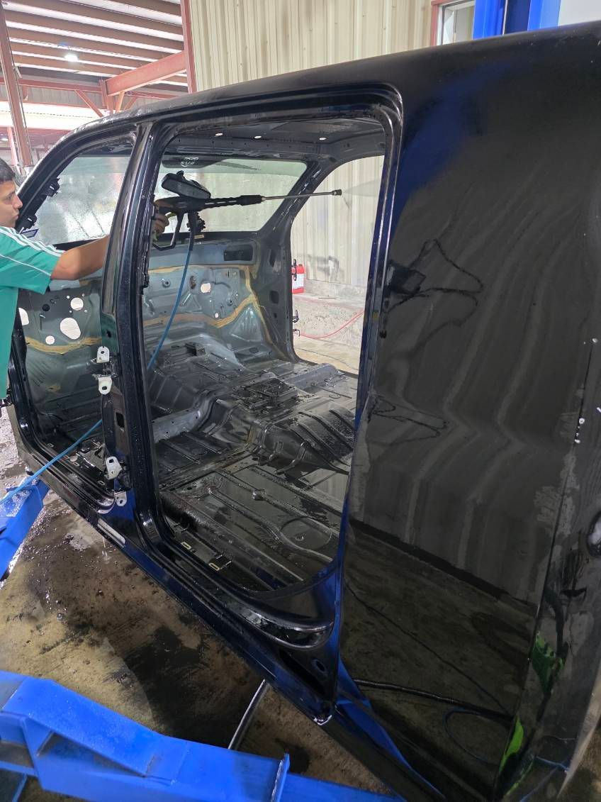 Black car door and side panel in a workshop, with blue tape and visible damage on the body.