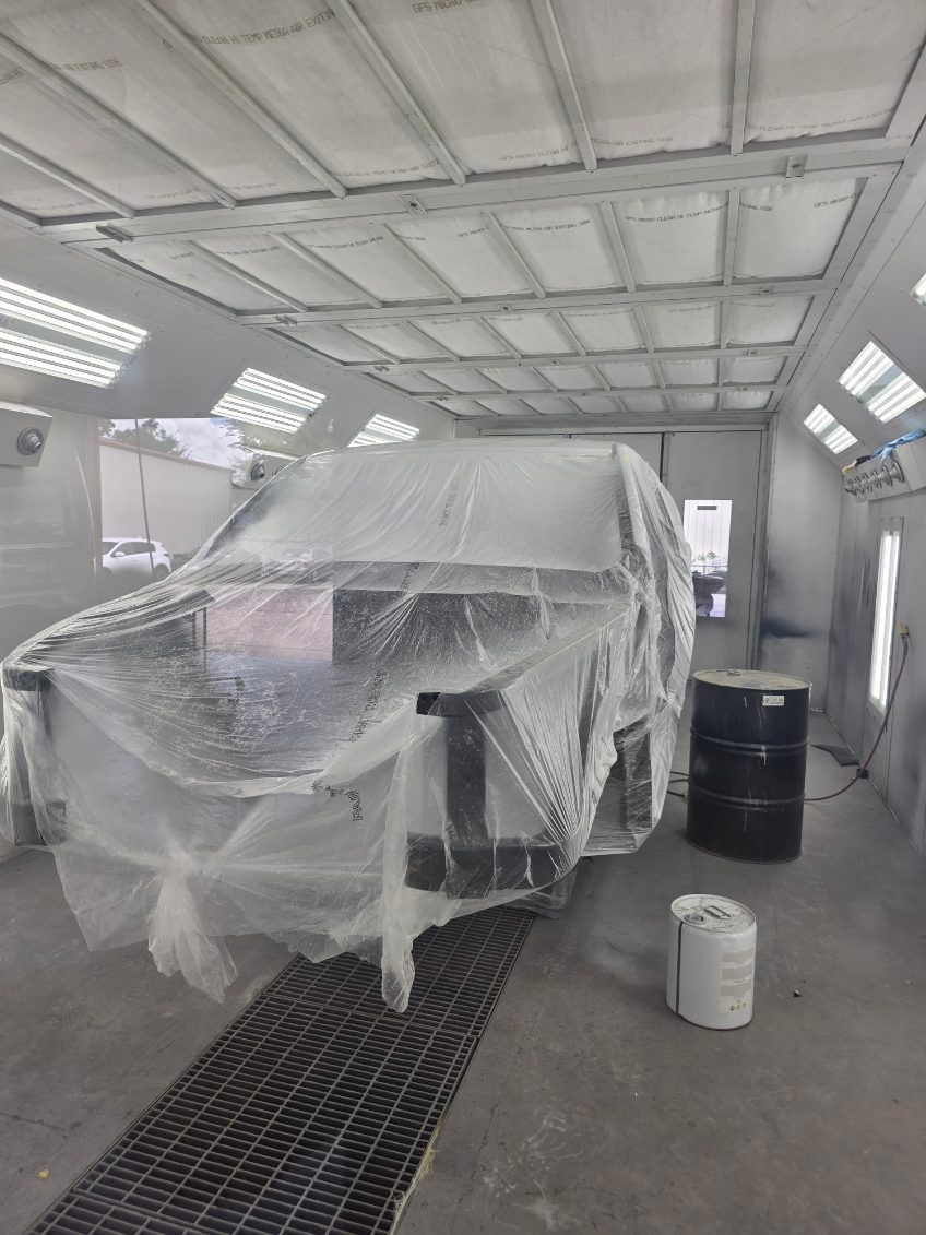 Car covered in plastic sheeting inside an auto paint booth, with paint cans nearby