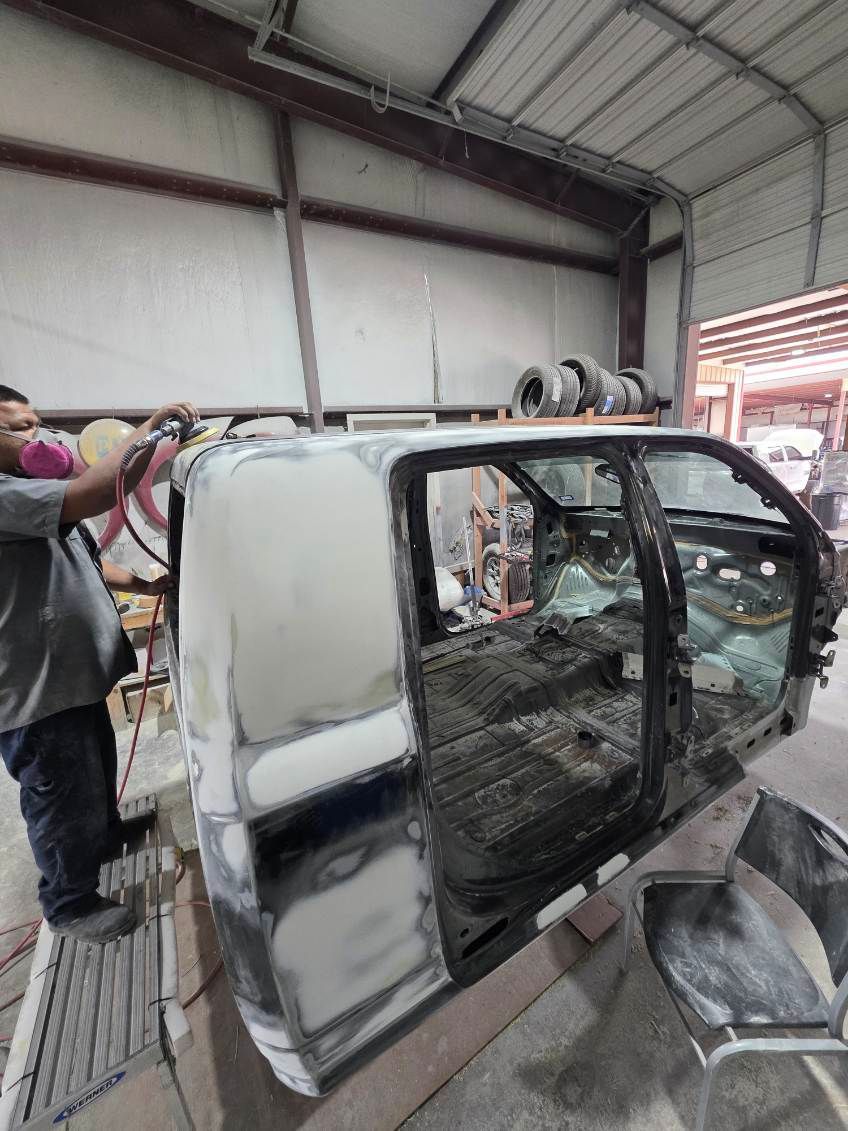 Person spray-painting a white vehicle body in a workshop