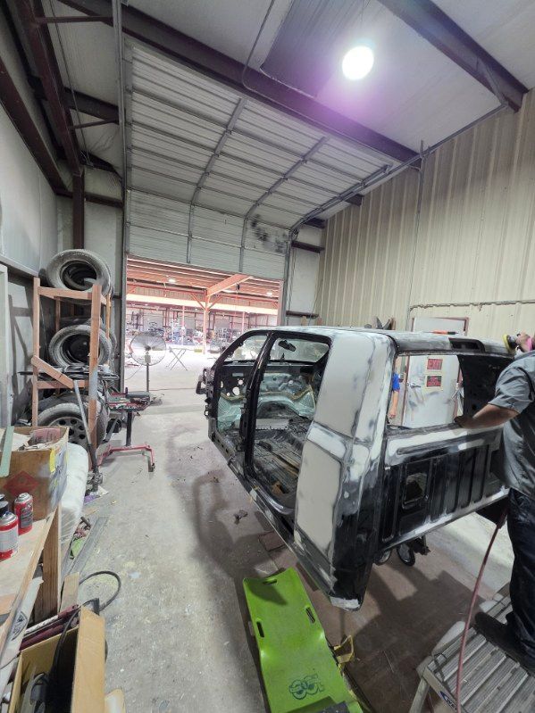 Damaged white van inside a cluttered auto repair garage with tools and parts stacked along the walls