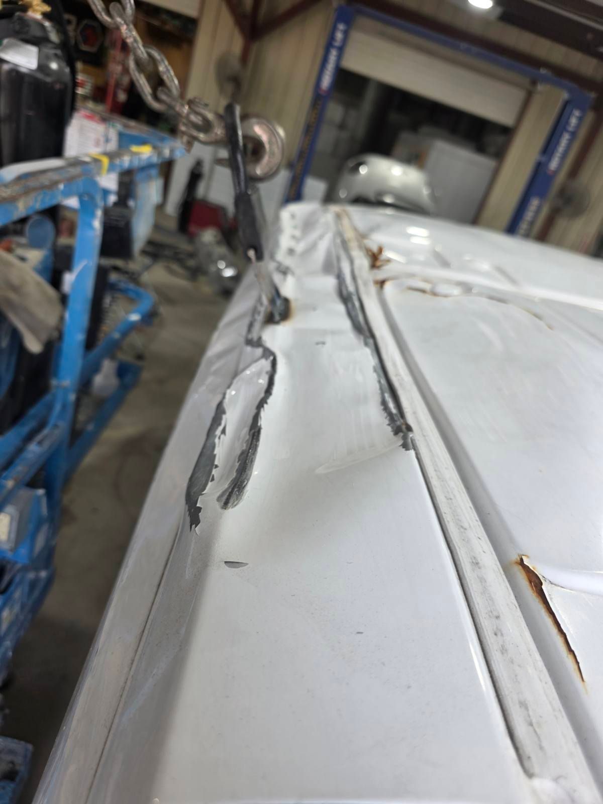 Close-up of a damaged white car roof with a dented seam in a workshop