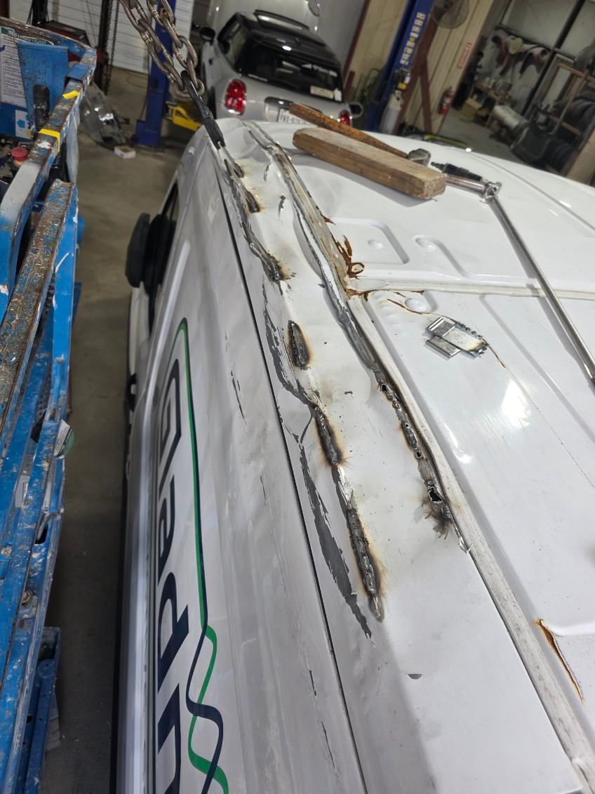 Damaged white vehicle in a garage, with peeling seams and exposed rust along the roofline.