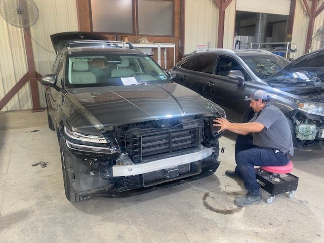 Mechanic kneeling beside black SUV in garage, inspecting the front bumper during repair