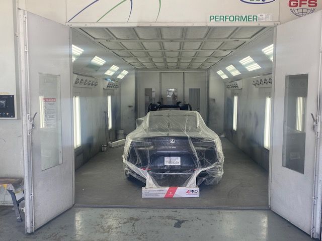 Car wrapped in plastic inside a white paint booth with open doors and bright overhead lights