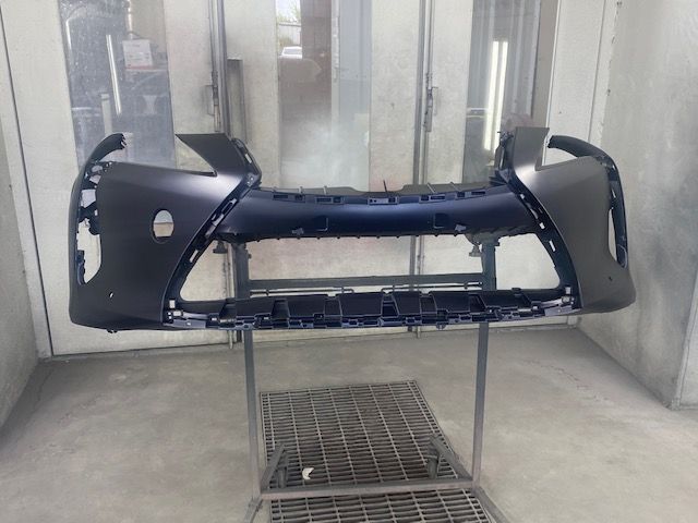 Black car bumper hanging in a spray booth, ready for painting or repair.