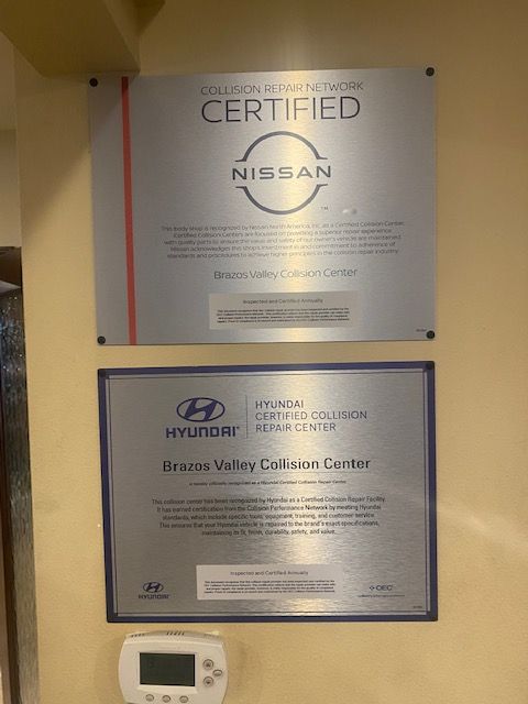 Wall-mounted Nissan and Hyundai certified service plaques on a beige wall, with a small thermostat below.