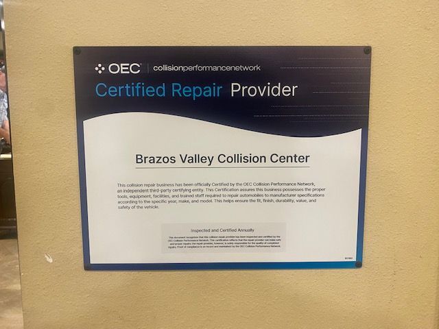 Framed blue “Certified Repair Provider” sign for Brazos Valley Collision Center on a beige wall