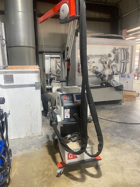 Industrial machine in a workshop, with black hoses hanging from an orange overhead beam.