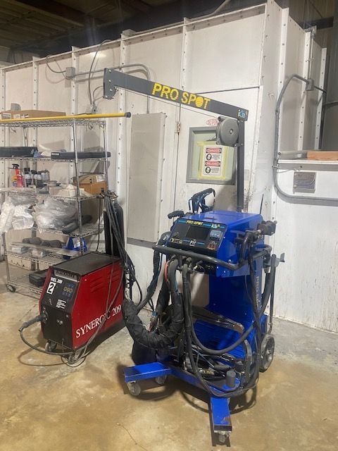 Garage workspace with a blue Pro Spot frame machine, red welder, and shelves of tools