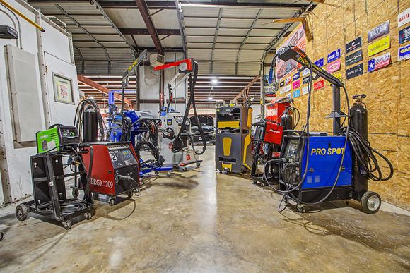 Industrial workshop with welding machines, tools, and equipment arranged around a concrete floor and metal roof