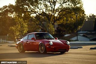 Red vintage sports car parked on a sunlit street with trees in the background