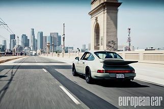 White sports car driving on a bridge with a city skyline in the background