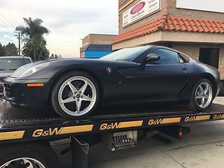 Black Ferrari on a tow truck in front of a building at sunset
