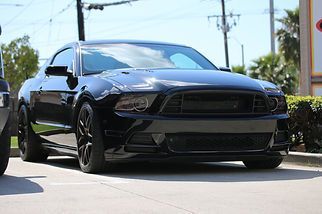 Black sports coupe parked on a sunny street, viewed from the front.