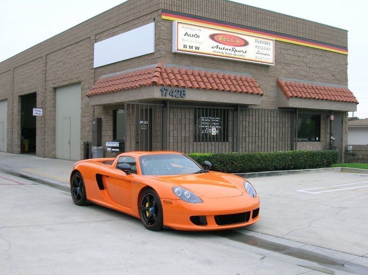 Orange sports car parked outside a brick commercial building with red awnings