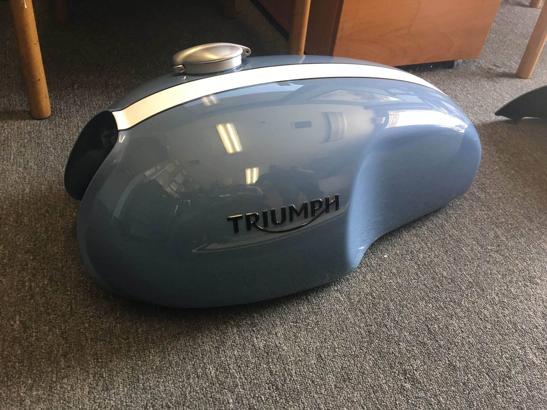 Blue Triumph motorcycle fuel tank on a carpeted floor
