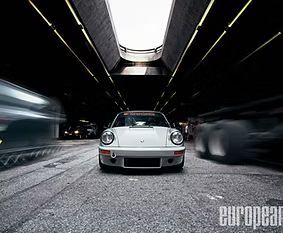 White sports car centered in a tunnel, flanked by blurred moving cars on both sides.