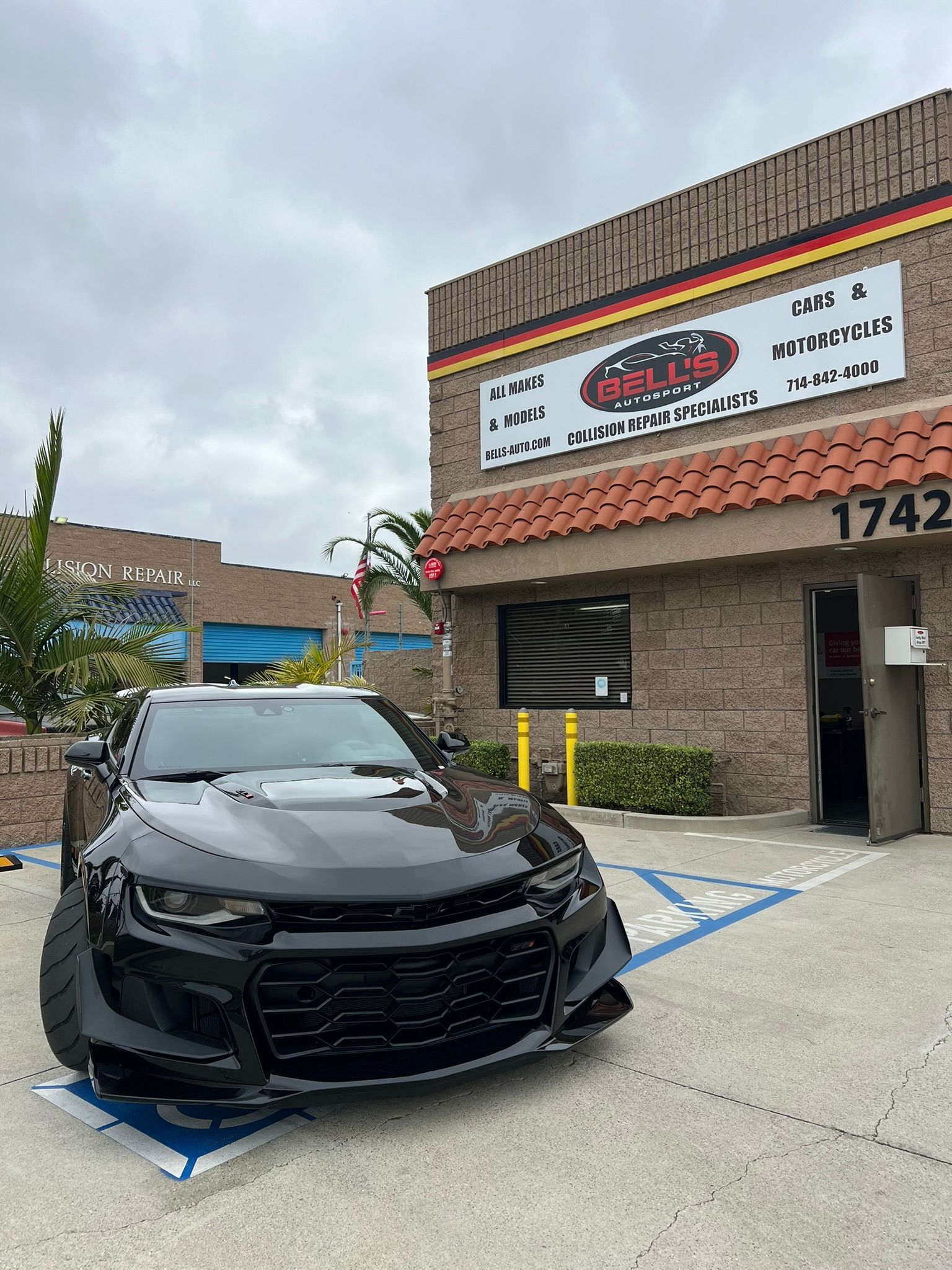 Black car parked in a handicap spot outside a storefront with a red awning and sign.