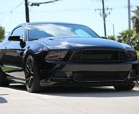 Black sports car driving on a sunny street, front view