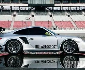 Silver Porsche 911 race car with BBI Autosport branding parked at a track, shown in side profile with reflections.