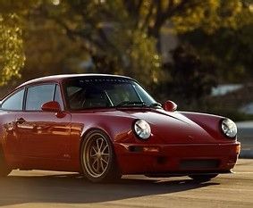 Red classic sports car parked outdoors in warm sunlight with trees in the background