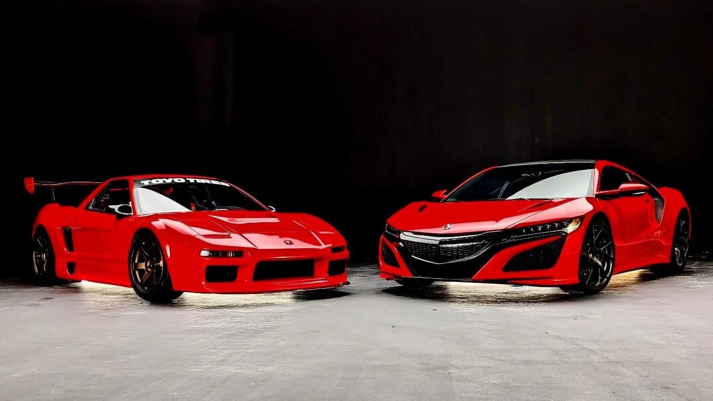 Two red sports cars parked side by side on a dark showroom floor, front views visible