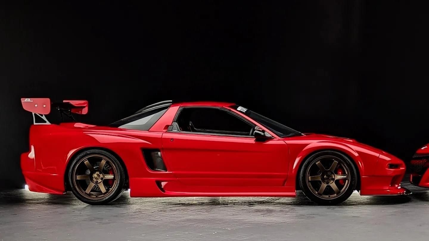 Red sports car with large rear wing, shown in side view on a dark studio background.