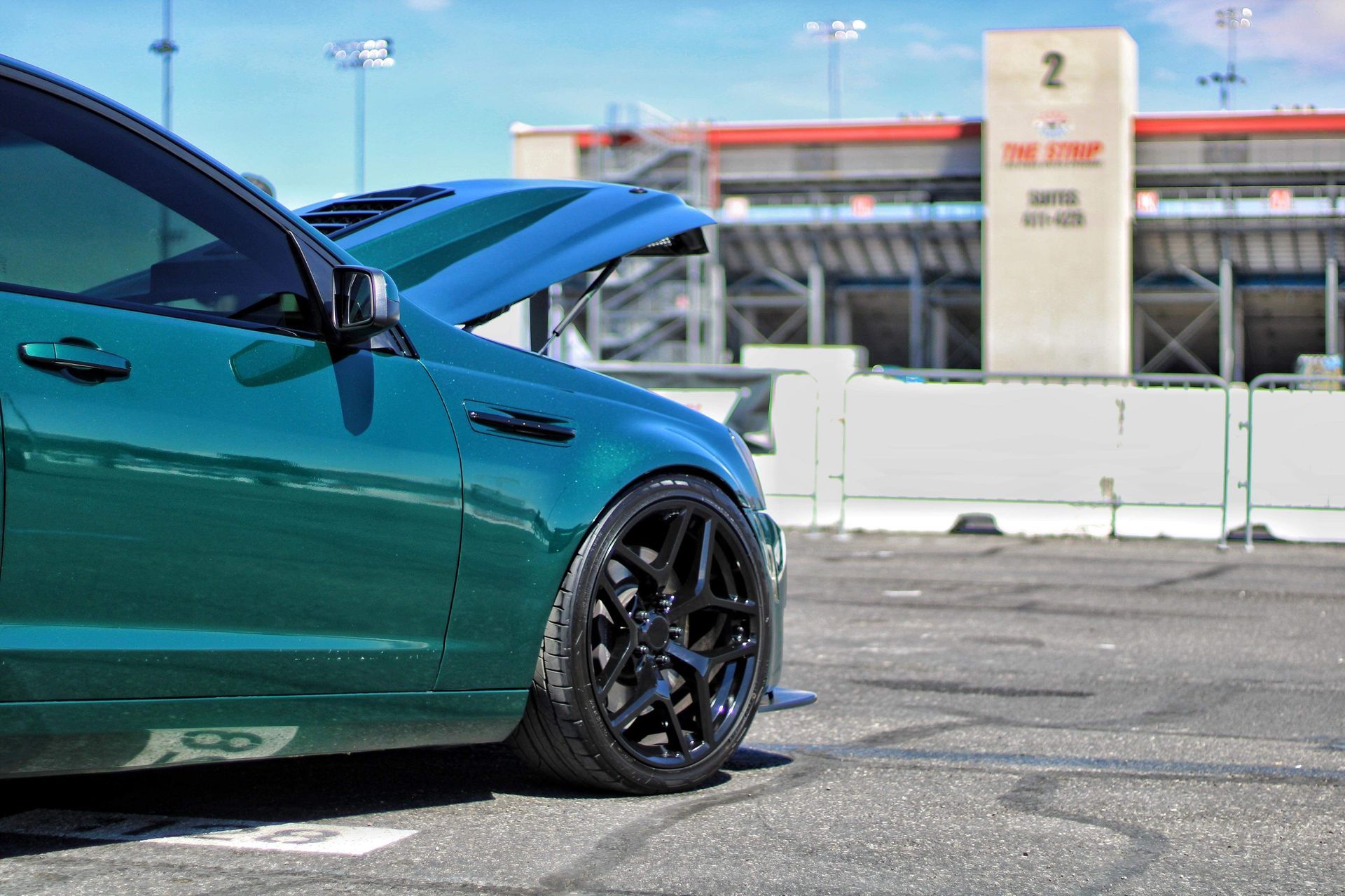 Teal sports car with black rims parked outdoors near a racetrack wall