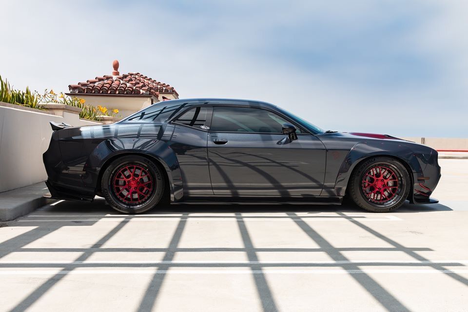 Black sports coupe with red rims parked on a sunlit driveway, side view.