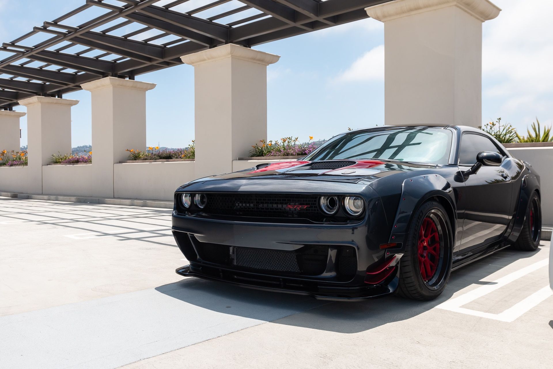 Black Dodge Challenger parked under a pergola on a sunny rooftop driveway