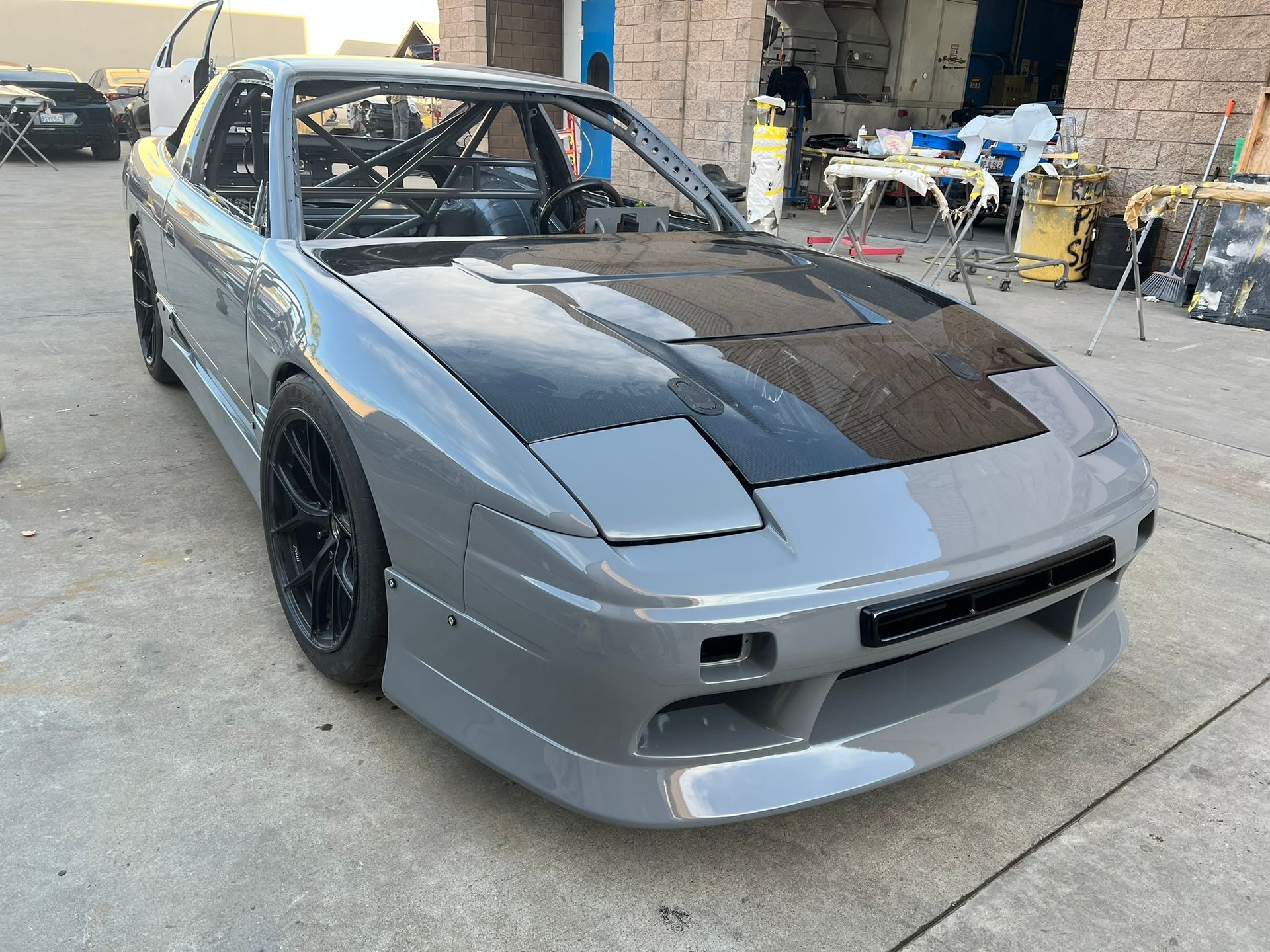 Gray modified sports car with black hood parked in a garage workshop